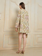 A woman stands indoors facing away, wearing the Social Queen Italian Baroque Floral Metallic Jacquard Jacket for a touch of vintage charm, paired with heeled sandals and carrying a small handbag.