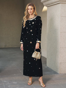 A woman stands on a stone floor in the Social Queen Jewel-Beaded Gold-Trim Dress with gold sandals, a woven handbag, and jewelry.
