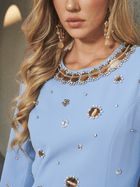 A woman in the Social Queen Jewel-Beaded Gold-Trim Dress, featuring light blue hand beadwork and gold rhinestone accents, with matching gold earrings; her face is partially visible.