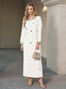 A woman stands outdoors wearing the Social Queen Jewel-Beaded Gold-Trim Dress, paired with gold earrings, gold heels, and holding a small gold purse.