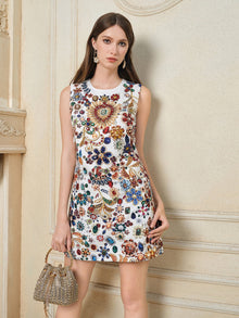 A woman wears the Social Queen Jewel-Embellished Floral Mini Dress and holds a small embellished handbag as she stands against a cream-colored, decorated wall.