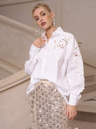 A woman in elevated casual elegance wears the Social Queen Lace Appliqué Shirt and a sequined skirt, posing before a beige staircase and looking at the camera.