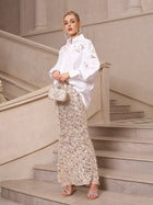 A woman poses on a staircase in an elevated casual look, wearing Social Queen’s Lace Appliqué Shirt paired with a silver sequin skirt, silver heels, and carrying a beaded handbag.