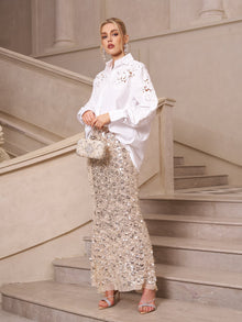 A woman poses on a staircase in an elevated casual look, wearing Social Queen’s Lace Appliqué Shirt paired with a silver sequin skirt, silver heels, and carrying a beaded handbag.