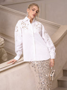 A woman in the Social Queen Lace Appliqué Shirt poses by a staircase, holding a round clutch bag—an effortless display of elevated casual elegance.