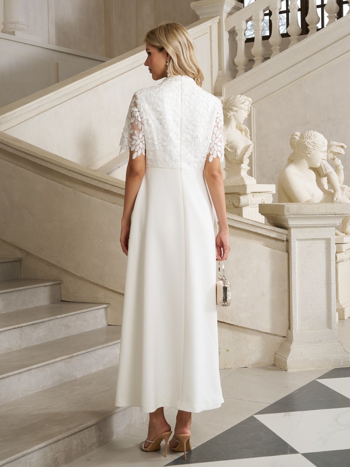 A woman in the Social Queen Lace-Panel Satin A-Line Gown stands on a marble staircase, holding a small purse, surrounded by statues and ornate railings.