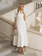 A woman wearing the Lace-Panel Satin A-Line Gown by Social Queen stands on a staircase, holding a small embellished handbag. A marble statue and ornate railing appear in the background.