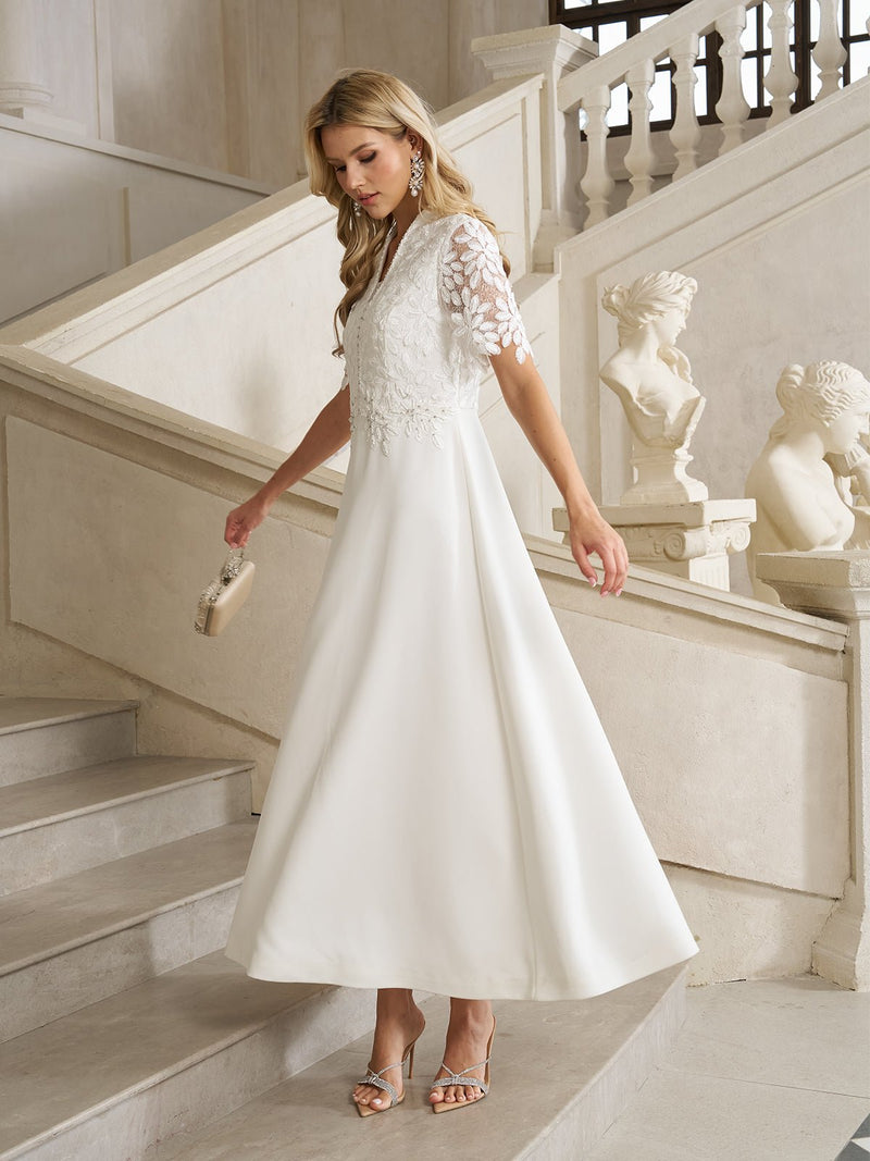 A woman wears the Social Queen Lace-Panel Satin A-Line Gown in ivory, standing on stone stairs with a clutch purse, classical statues, and ornate railings in the background.