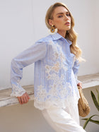 A woman models the Social Queen Lace Panel Striped Cotton Blouse, featuring yarn-dyed stripes and lace details, styled with white pants, statement earrings, and a woven bag against a white wall.