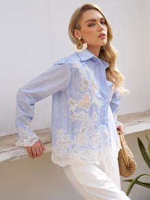 A woman models the Social Queen Lace Panel Striped Cotton Blouse, featuring yarn-dyed stripes and lace details, styled with white pants, statement earrings, and a woven bag against a white wall.