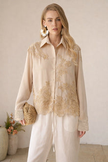 A woman models the Social Queen Lace Panel Striped Cotton Blouse with white pants and a woven clutch, posed indoors against a neutral background with a vase of flowers.