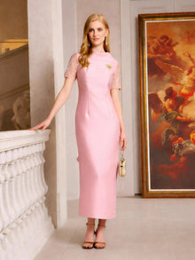 A woman in the Social Queen Lace-Trim Satin Midi Dress, a fitted pale pink style with lace cape sleeves, stands indoors beside a railing and a large framed painting.