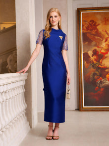 A woman in the Social Queen Lace-Trim Satin Midi Dress stands indoors next to a white railing and large framed painting, holding a small purse.