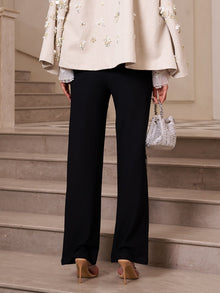 A person stands on stone steps in Social Queen's Lace-Trim Straight-Leg Trousers, a beige embellished top, nude heels, and a silver handbag—offering chic inspiration for wedding guest attire.