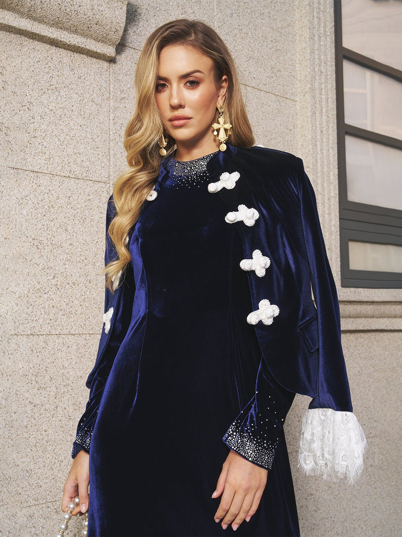 A woman wears the Social Queen Lace-Trim Velvet Jacket, showcasing blue high-density velvet with white lace details and an East-meets-West style, as she stands by a stone wall and window.
