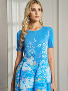 A woman with long blonde hair and statement earrings wears the Social Queen Lake Blue Print Plissé A-Line Dress, posing indoors against a light-colored wall and door.