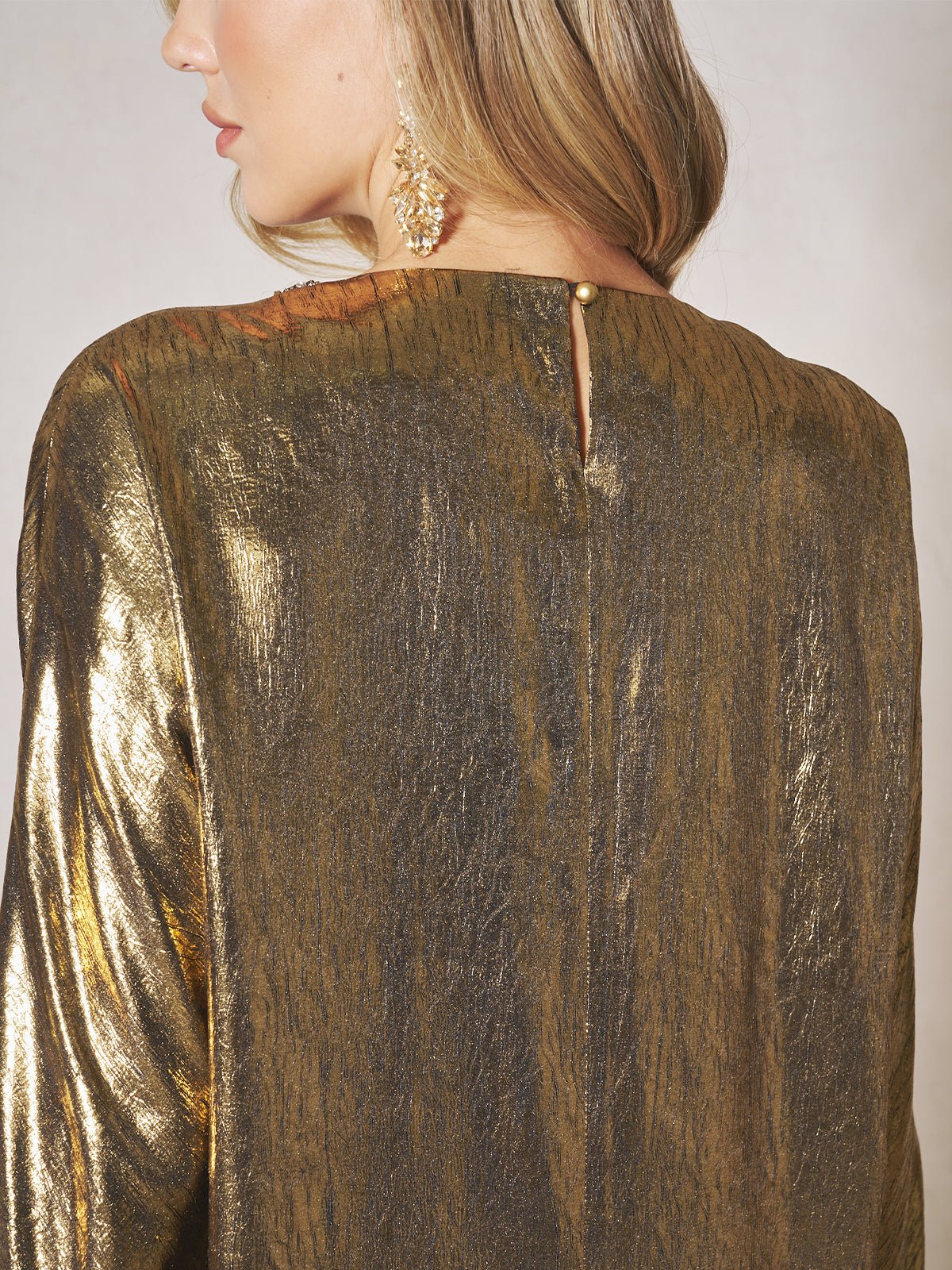 A woman is seen from behind wearing the Social Queen Metallic Crystal-Embellished Slit Dress, featuring an elegant metallic finish and button closure at the back. She has long hair and a dangling earring.