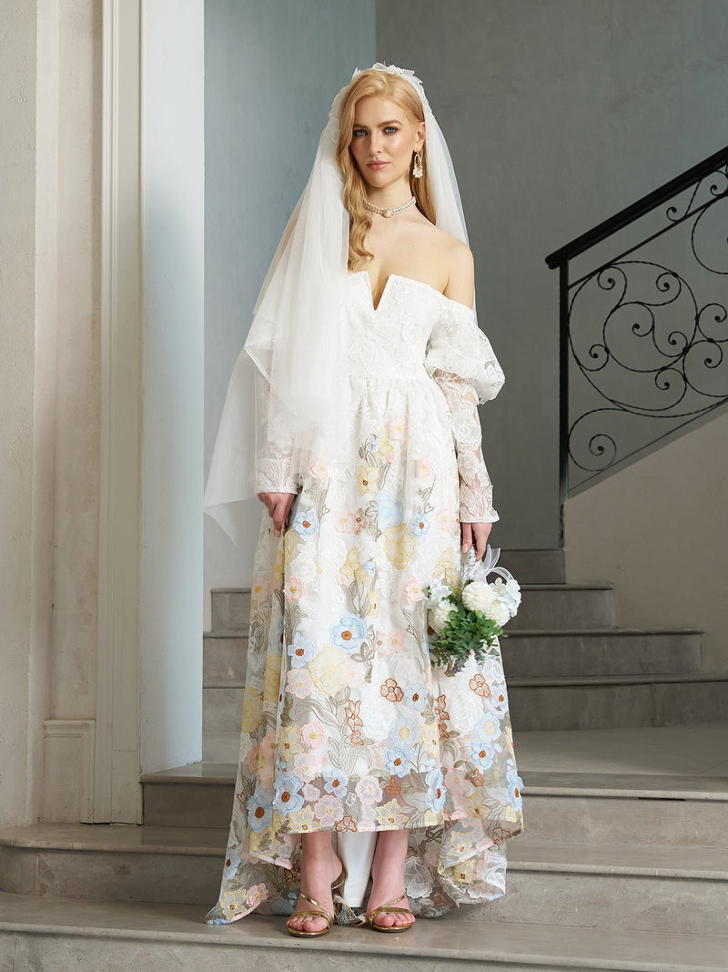 A woman stands on a staircase wearing the Social Queen Off-Shoulder Floral Embroidered Lace Gown with Veil, holding a bouquet.