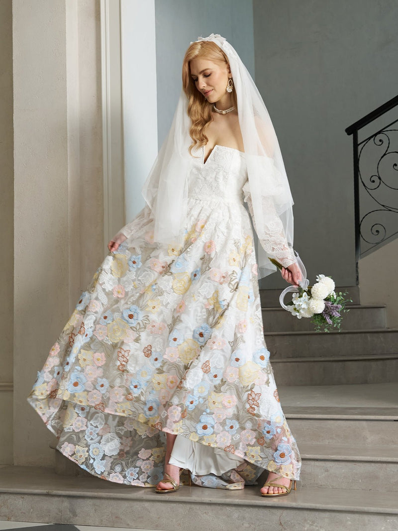 A bride wears the Social Queen Off-Shoulder Floral Embroidered Lace Gown with Veil, standing on stairs and holding a bouquet of white and purple flowers in one hand.