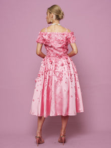 A woman, seen from behind, wears the Social Queen Off-Shoulder Floral Satin Gown with 3D floral details and pink heels, standing before a plain pink backdrop.