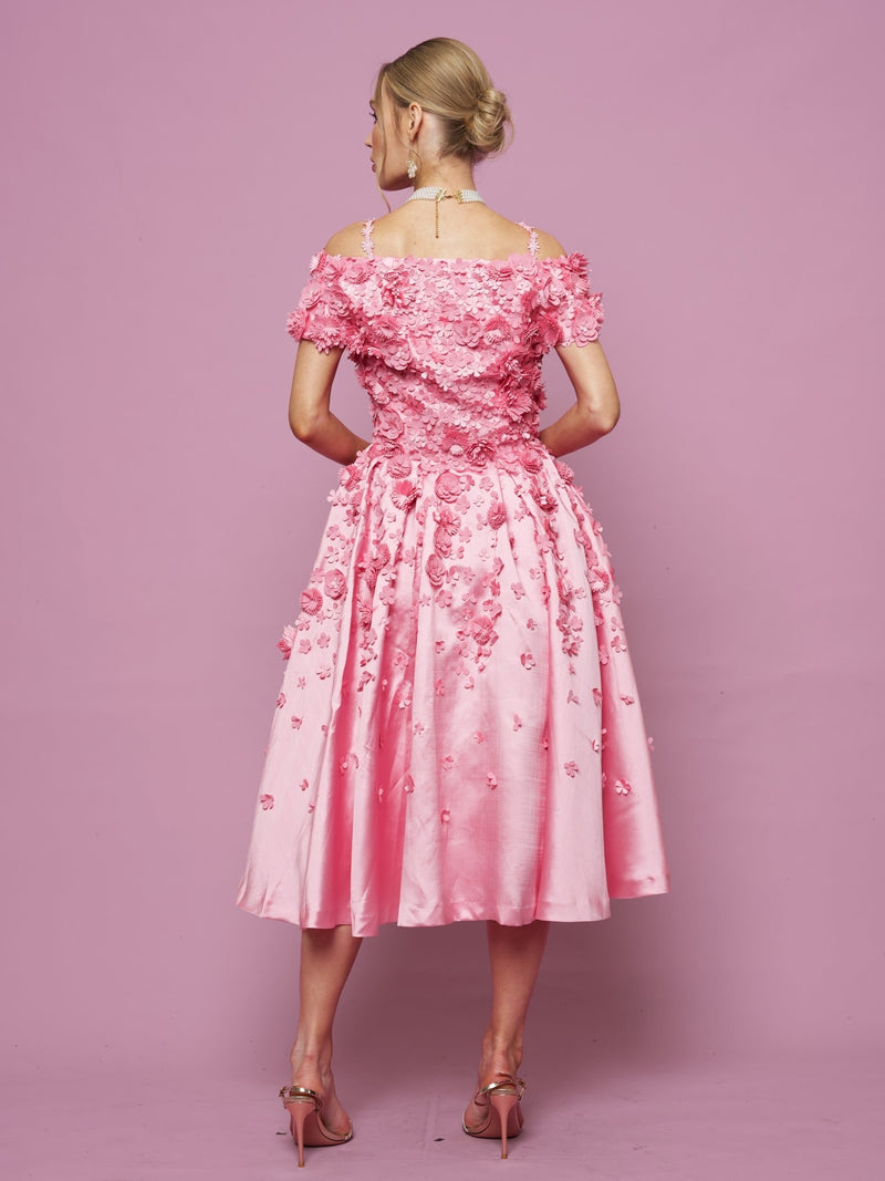 A woman, seen from behind, wears the Social Queen Off-Shoulder Floral Satin Gown with 3D floral details and pink heels, standing before a plain pink backdrop.