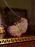 The Social Queen Ombré Crystal Butterfly Mini Bag, featuring a chain strap, rests on polished wood with gold detailing in front of a framed picture—a dazzling evening clutch ideal as a wedding accessory.