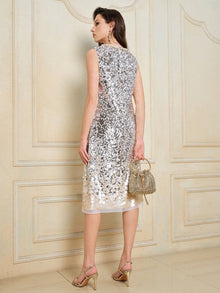 A woman wears the Social Queen Ombre Silver & Gold Sequin Embellished Dress, featuring a sleeveless mid-length design with a diamond-trimmed neckline, paired with heeled sandals and a small textured handbag, in a cream-paneled room.