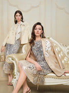 Two women showcase the Social Queen Ombre Silver & Gold Sequin Embellished Dress, featuring sparkling details and a diamond-trimmed neckline, as they pose indoors by a cream ornate sofa against a beige wall.