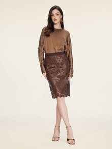 A woman stands against a plain background wearing a brown satin blouse, strappy heels, and the Social Queen Openwork Embroidered Leather Skirt.