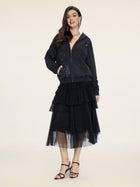 A woman stands against a plain background wearing an embellished black zip-up hoodie, the Social Queen Organza Pleated Skirt, and black strappy heels.