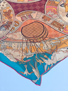 The Social Queen Original Pattern Print Silk Scarf showcases a whimsical, colorful bird and hot air balloon motif with geometric and architectural details on blue—an ideal wedding guest accessory.