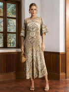 A woman stands indoors wearing the Social Queen Paisley Print Pleated Midi Dress with flared sleeves, holding a woven handbag and pairing it with strappy sandals.