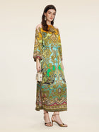 A woman wears the Social Queen Paisley Printed Silk Satin Dress in yellow, green, and brown, paired with a small white handbag and gold sandals.