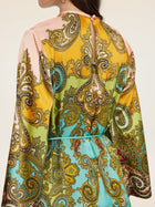 A woman is seen from the back wearing the Social Queen Paisley Printed Silk Satin Dress featuring long sleeves and a vibrant yellow, green, blue, and pink paisley pattern inspired by vintage styles.
