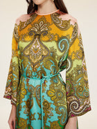 A person wearing the Social Queen Paisley Printed Silk Satin Dress, a vintage-inspired long-sleeved piece with hand-printed yellow, green, and turquoise paisley patterns, cinched at the waist with a thin belt.