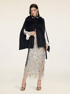 A woman wears the Social Queen Pearl & 3D Floral Couture Cape, paired with a white blouse, silver sequin fringed skirt, and strappy high heels against a plain background.