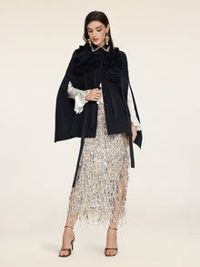 A woman wears the Social Queen Pearl & 3D Floral Couture Cape, paired with a white blouse, silver sequin fringed skirt, and strappy high heels against a plain background.