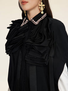 A woman models the Social Queen Pearl & 3D Floral Couture Cape, featuring layered black 3D floral ruffles and pearls. She also wears ornate gold earrings, with her face partially out of frame.