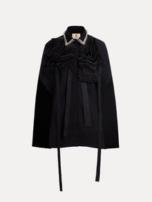 The Social Queen Pearl & 3D Floral Couture Cape features couture craftsmanship with textured ruffle detailing, long neck ties, and a pearl-embellished collar, shown against a plain white background.