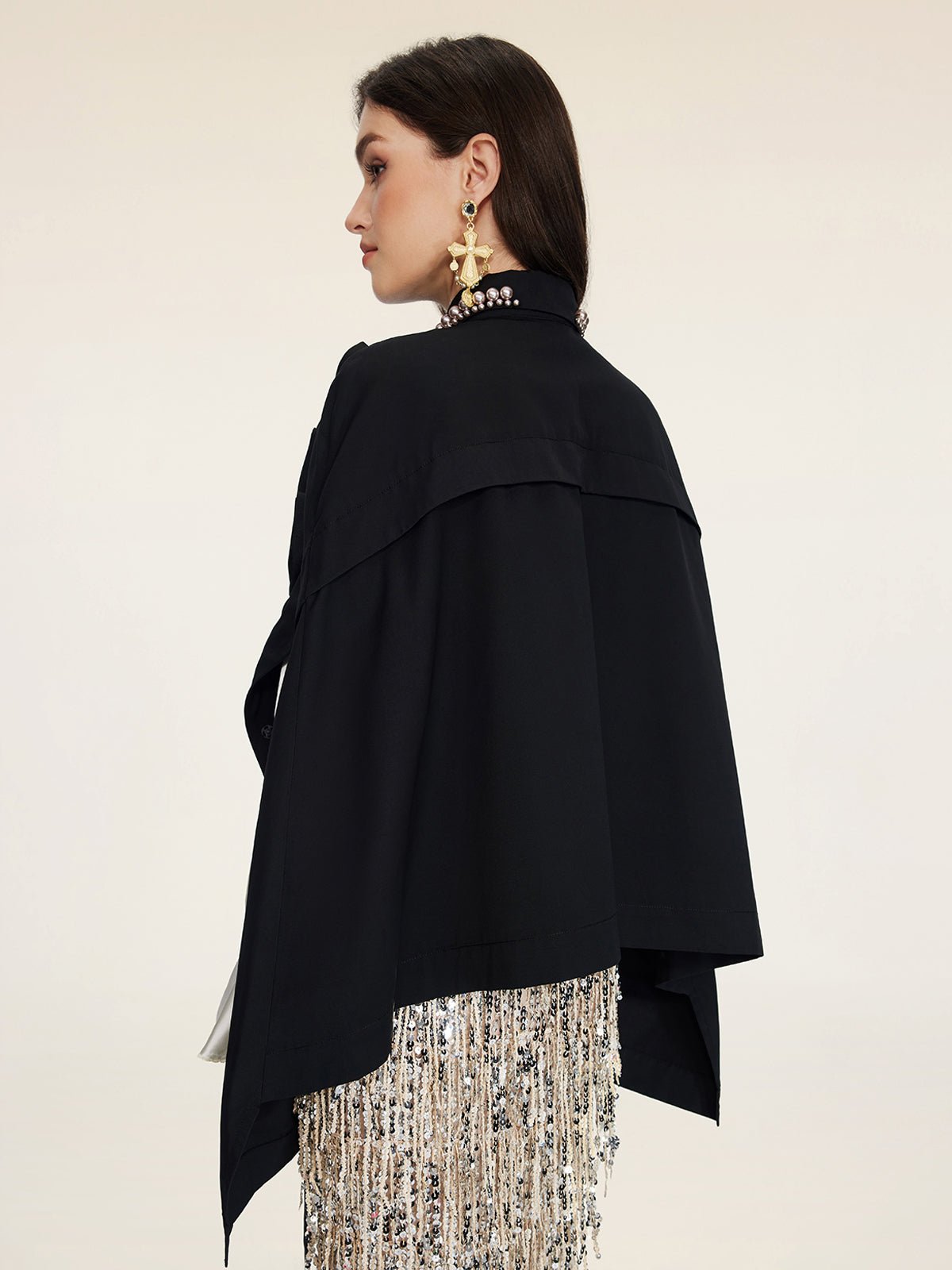 A woman in profile models the Pearl & 3D Floral Couture Cape by Social Queen, featuring beaded fringe details and large star-shaped earrings, highlighting couture craftsmanship against a plain background.