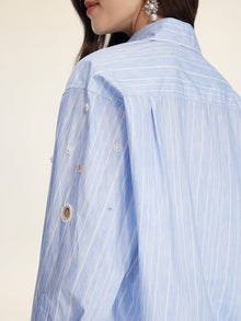 A woman wears the Pearl & Beaded Striped Blouse by Social Queen, featuring light blue pinstripes and hand-applied pearls on the sleeve, shown from the side and back.