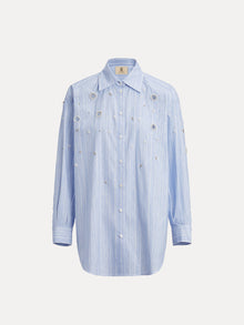 The Pearl & Beaded Striped Blouse by Social Queen is a light blue, long-sleeve top with subtle vertical stripes, a relaxed fit, and hand-applied pearls and metallic embellishments on the front.