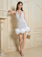 A woman stands indoors wearing the Social Queen Pearl-Crystal Embellished Floral Hem Mini Dress, styled with a small beaded handbag and silver sandals.