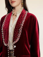 A woman wears Social Queen's Pearl & Crystal Velvet Blazer in deep red, its jeweled trim adding vintage glamour over a textured cream blouse, finished with gold jewelry and drop earrings.