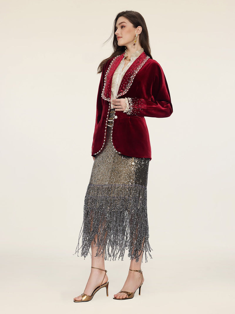 A woman stands in profile against a plain background, wearing Social Queen’s Pearl & Crystal Velvet Blazer styled over a metallic fringed skirt and gold heeled sandals.