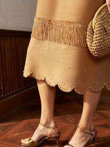 A person wearing the Social Queen Pearl Detail Fringe Pleated Dress with gold high-heeled sandals and holding a woven straw bag.