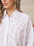 A woman wears the Social Queen Pearl-Embellished Floral Blouse with ornate gold earrings—a chic choice for a wedding guest.