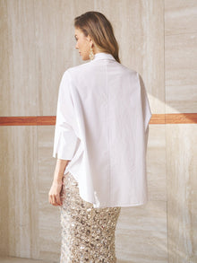 A person stands indoors, facing away, wearing the Social Queen Pearl-Embellished Floral Blouse with a beige tiled wall in the background.