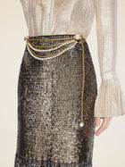 A person wears a shimmery blouse with flared cuffs and the Social Queen Pearl-Trim Sequin Fringe Skirt, accessorized with layered pearl chain waist belts.