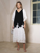 A woman stands indoors wearing the Social Queen Pearl-Trim Silk Velvet Dress with sheer sleeves, paired with silver heels, a sparkling necklace, and a small silver handbag—a sophisticated wedding guest look.